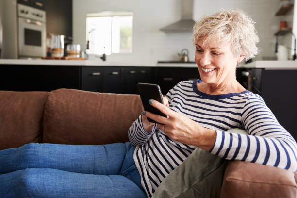istock Senior white woman sitting on couch at home using smartphone 1047528446