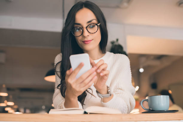 istock pretty young woman in eyeglasses using smartphone at table with coffee cup in cafe 1047528514