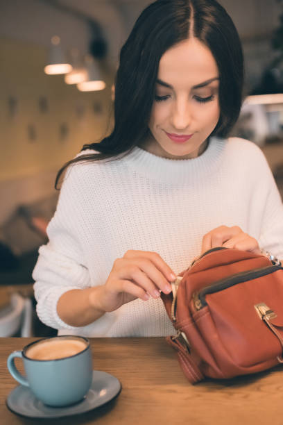 istock attractive woman pulling out cash from bag at table with coffee cup in cafe 1047528592