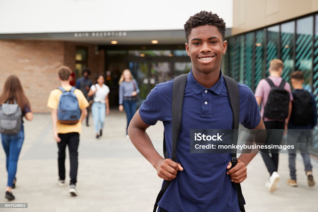 Portrait Of Smiling männlich High Student außen College Schulgebäude mit anderen Jugendlichen Studenten im Hintergrund - Lizenzfrei Teenager-Alter Stock-Foto