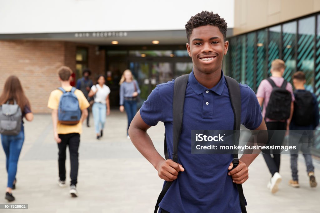 Retrato de sonriente hombre alto estudiante exterior Colegio el edificio de escuela con otros estudiantes adolescentes en fondo - Foto de stock de Adolescente libre de derechos