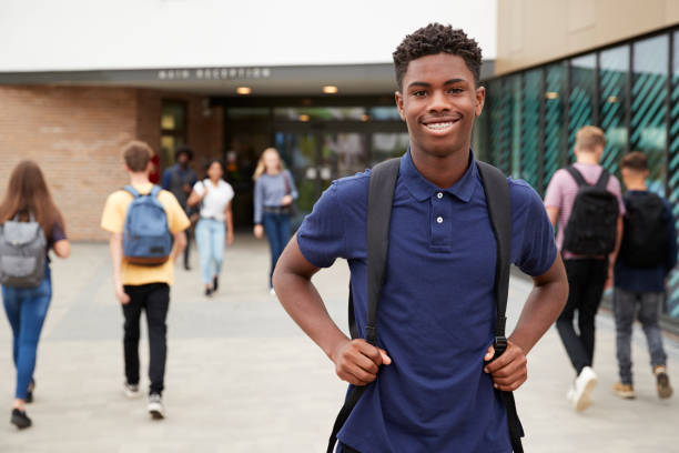 portret uśmiechniętego mężczyzny ucznia szkoły średniej poza budynkiem college'u z innymi nastoletnimi uczniami w tle - teenage boys zdjęcia i obrazy z banku zdjęć