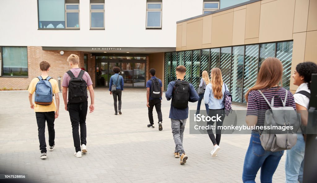 Vista traseira de estudantes secundaristas, entrando no prédio de faculdade juntos - Foto de stock de Escola royalty-free