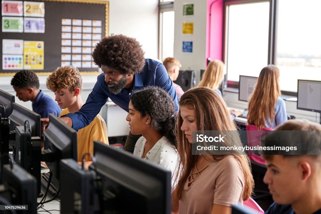 Male Teacher Helping Teenage Female High School Student Working In Computer Class Classroom Stock Photo