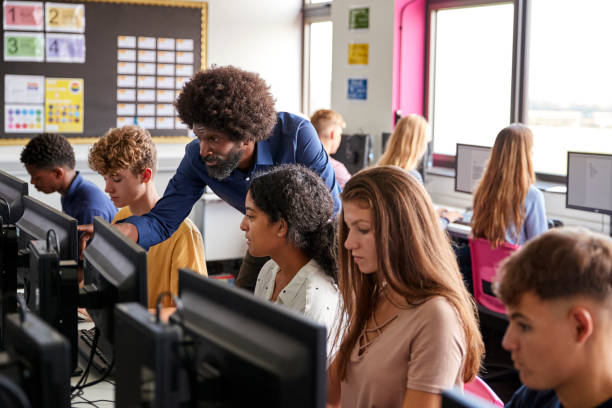 male teacher helping teenage female high school student working in computer class - teacher computer high school student classroom imagens e fotografias de stock