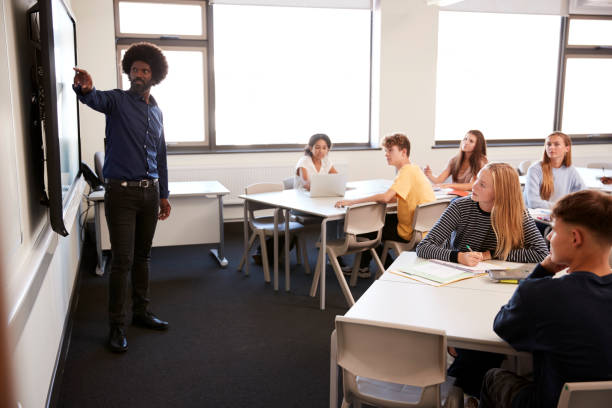 istock Male High School Teacher Standing Next To Interactive Whiteboard And Teaching Lesson 1047530098