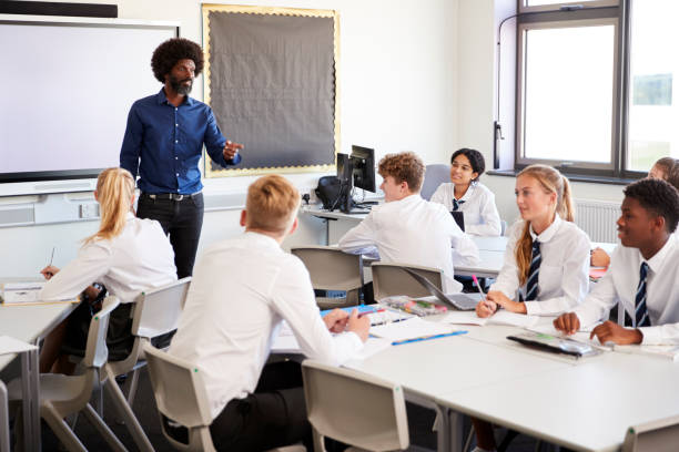 istock Male High School Teacher Standing Next To Interactive Whiteboard And Teaching Lesson To Pupils Wearing Uniform 1047532598