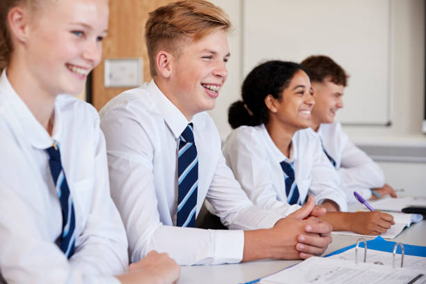 Line Of High School Students Wearing Uniform Sitting At Desk In Classroom Line Of High School Students Wearing Uniform Sitting At Desk In Classroom school uniform stock pictures, royalty-free photos & images