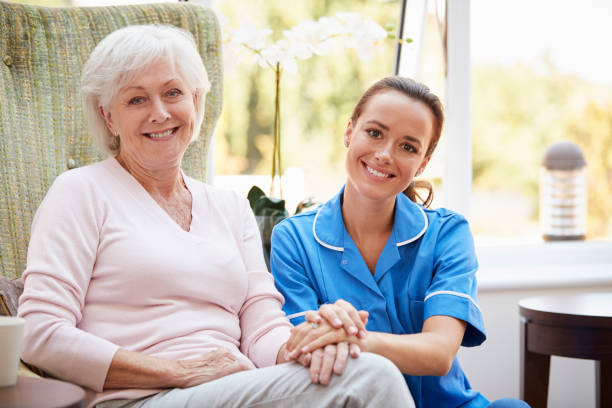 retrato de mujer mayor sentada en silla con enfermera en el hogar del jubilado - senior living communitiy fotografías e imágenes de stock