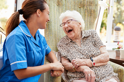Senior mujer sentada en la silla y riendo con la enfermera en el hogar del jubilado photo