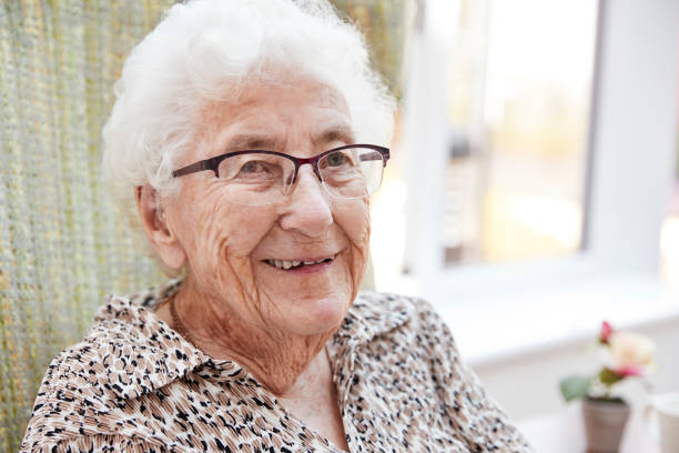 ritratto di donna anziana seduta sulla sedia nel salotto della casa di riposo - smiling women glasses assistance foto e immagini stock