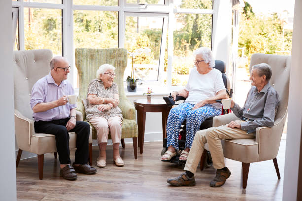 los residentes masculinos y femeninos sentados en sillas y hablando en el salón del hogar del jubilado - care community 80 plus years cheerful fotografías e imágenes de stock
