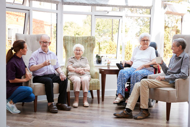 los residentes masculinos y femeninos sentados en sillas y hablando con el cuidador en el salón del hogar del jubilado - senior living communitiy fotografías e imágenes de stock