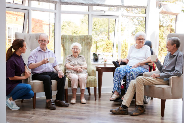 mieszkańcy płci męskiej i żeńskiej siedzą na krzesłach i rozmawiają z opiekunem w salonie domu spokojnej starości - one person lifestyles 80 plus years indoors zdjęcia i obrazy z banku zdjęć