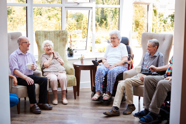 los residentes masculinos y femeninos sentados en sillas y hablando en el salón del hogar del jubilado - senior living communitiy fotografías e imágenes de stock