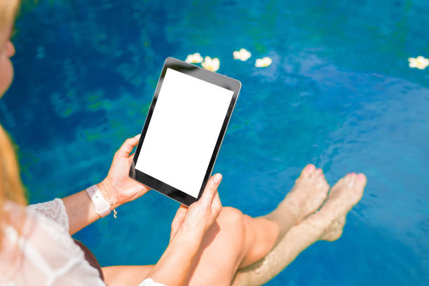 istock Woman sitting by the pool and using tablet computer. Vertical screen orientation. 1047540314