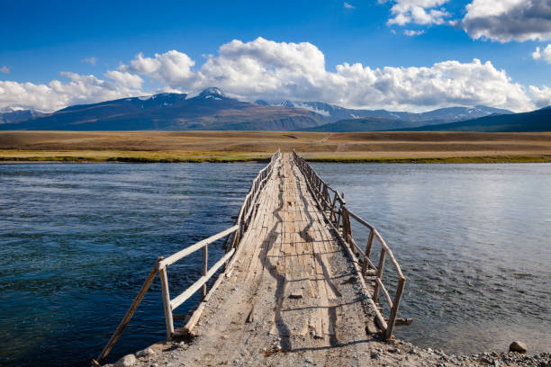 Shabby wooden bridge over a river with distant mountain range in background, Altai Mountains, Western Mongolia