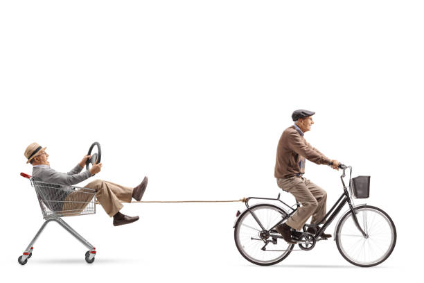 istock Elderly man riding a bicycle and pulling a shopping cart with a man holding a steering wheel 1047545066