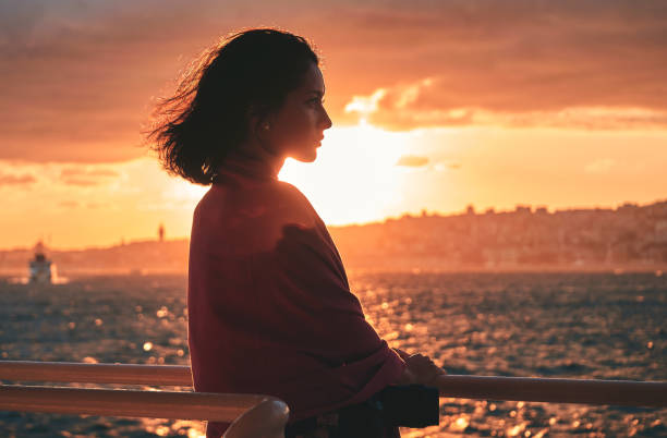 beautiful woman standing on deck of cruise ship and looking away at sunset. stock photo