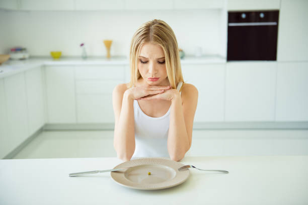 istock Stressed depressed upset unsatisfied with figure lady sitting at table in modern white light room indoors looking at empty big plate, waiting for tasty lunch snack, trying not to be nervous 1047561102