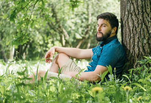 Young man listening to music in green summer forest and relaxing