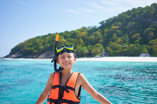 happy Asian boy wearing snorkel and preparing for swimming in summer vacation in Phuket, Thailand
