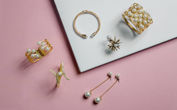 goldene armbänder und ohrringe mit perlen auf rosa und weißen hintergrund - gold earrings stock-fotos und bilder