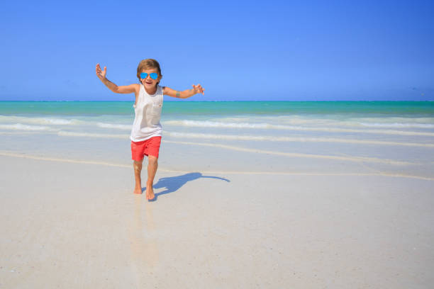 Happy child boy running along the beach with extended hands.