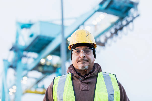 Hispanic dock worker at shipping port A mature Hispanic man in his 40s wearing a hard hat, safety vest and safety goggles, a dock worker working at a shipping port. gantry crane stock pictures, royalty-free photos & images