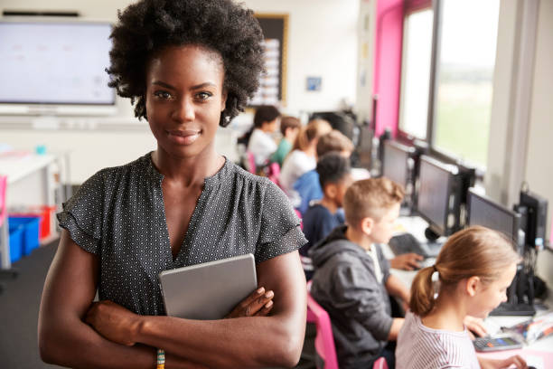 ritratto di insegnante donna che tiene in mano la linea di insegnamento di tablet digitali di studenti delle scuole superiori seduti accanto a schermi in classe informatica - studying child female student foto e immagini stock