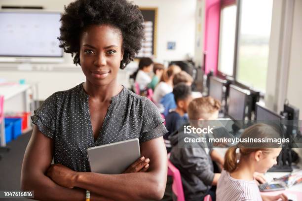 Portrait Of Female Teacher Holding Digital Tablet Teaching Line Of High School Students Sitting By Screens In Computer Class Stock Photo - Download Image Now