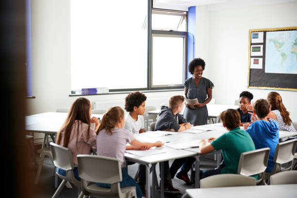 istock Female High School Tutor Standing By Table With Students Teaching Lesson 1047617282