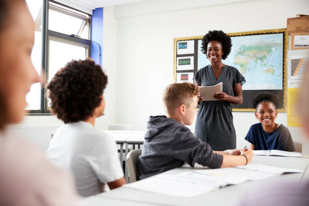 istock Female High School Tutor Standing By Table With Students Teaching Lesson 1047617354