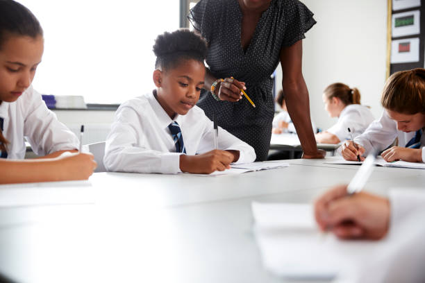 istock Female High School Tutor Helping Students Wearing Uniform Seated Around Tables In Lesson 1047617516