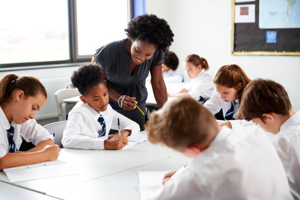 istock Female High School Tutor Helping Students Wearing Uniform Seated Around Tables In Lesson 1047617530