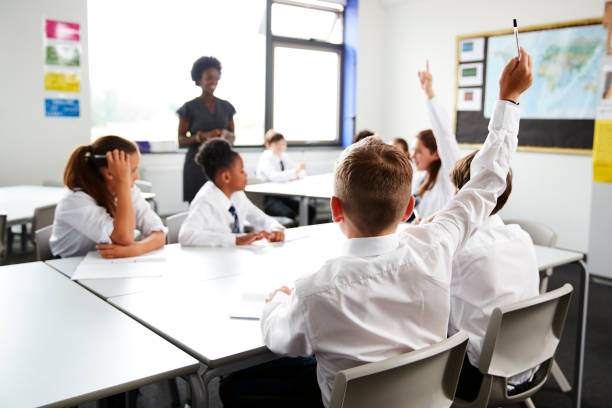 istock High School Students Wearing Uniform Raising Hands To Answer Question Set By Teacher In Classroom 1047617544