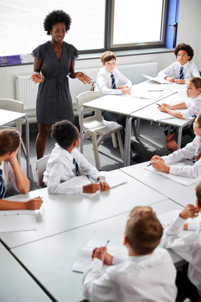 istock Female High School Tutor Helping Students Wearing Uniform Seated Around Tables In Lesson 1047617552