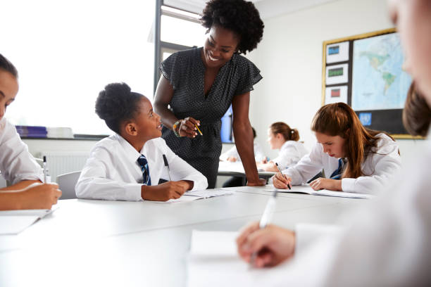 istock Female High School Tutor Helping Students Wearing Uniform Seated Around Tables In Lesson 1047617608