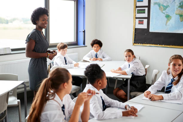 istock Female High School Tutor Helping Students Wearing Uniform Seated Around Tables In Lesson 1047617610