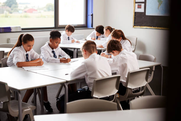 istock High School Students Wearing Uniform Sitting And Working Around Table In Lesson 1047617648