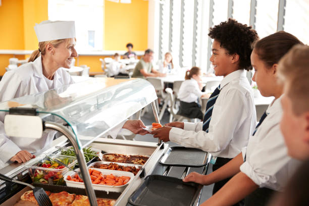High School Students Wearing Uniform Being Served Food In Canteen High School Students Wearing Uniform Being Served Food In Canteen cafeteria worker photos stock pictures, royalty-free photos & images