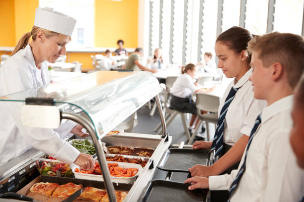 schülerinnen und schüler in uniform serviert essen in kantine - kantinenfrau stock-fotos und bilder