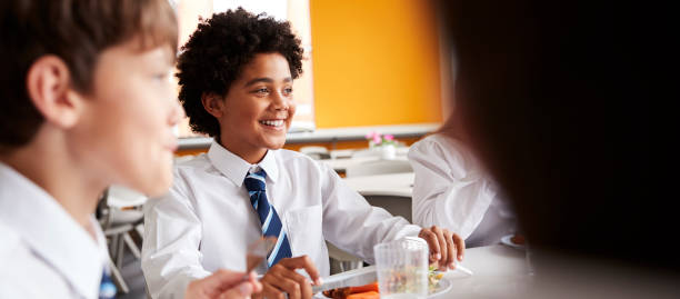 istock Group Of High School Students Wearing Uniform Sitting Around Table And Eating Lunch In Cafeteria 1047619486