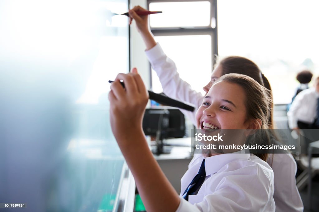 Female High School Students Wearing Uniform Using Interactive Whiteboard During Lesson Education Stock Photo