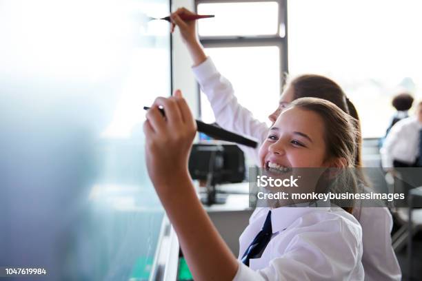 Female High School Students Wearing Uniform Using Interactive Whiteboard During Lesson Stock Photo - Download Image Now