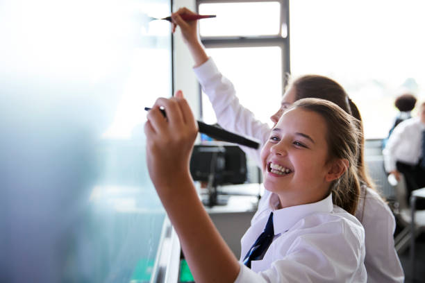 female high school students wearing uniform using interactive whiteboard during lesson - child education classroom student imagens e fotografias de stock