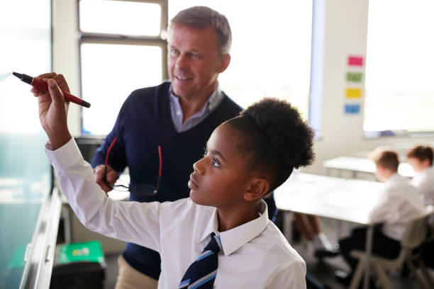 insegnante di scuola superiore maschile con studentessa che indossa l'uniforme usando la lavagna interattiva durante la lezione - educazione di scuola privata foto e immagini stock