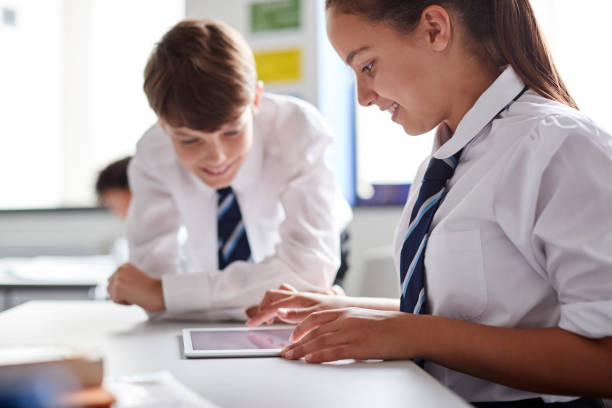 Two High School Students Wearing Uniform Working Together At Desk Using Digital Tablet Two High School Students Wearing Uniform Working Together At Desk Using Digital Tablet independent school education stock pictures, royalty-free photos & images