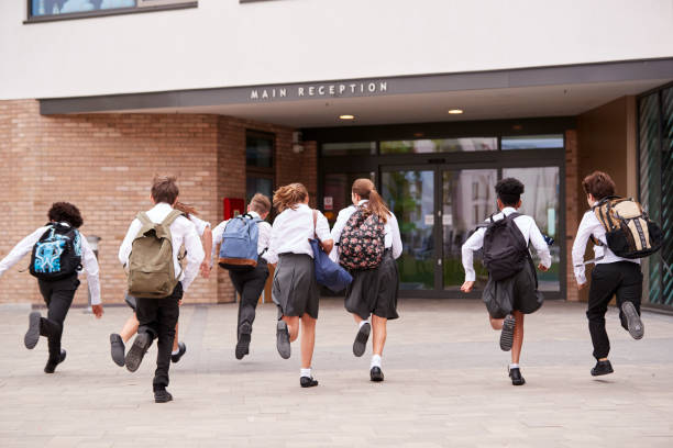 istock Group Of High School Students Wearing Uniform Running Into School Building At Beginning Of Class 1047620590