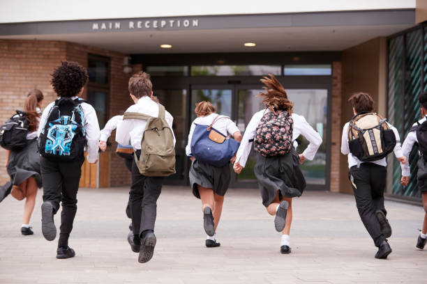 Group Of High School Students Wearing Uniform Running Into School Building At Beginning Of Class Group Of High School Students Wearing Uniform Running Into School Building At Beginning Of Class independent school education stock pictures, royalty-free photos & images